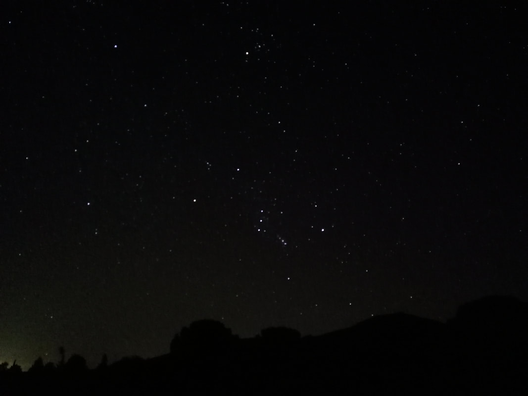 Se ve un cielo estrellado, con la constelación de Orión abajo y las Híades de Tauro encima. Orión es la figura de un cazador, formado por un triángulo irregular de estrellas bastante brillantes en la cabeza, un cinturón de tres estrellas muy juntas en la zona de la cadera y dos estrellas también muy brillantes como pies. En el muslo, brilla un pequeño cúmulo de luces que parecen formar un puñal (allí se encuentra la Gran Nebulosa de Orión, M42), y al frente parece sujetar un escudo de estrellas. Las Híades, por su parte, forman un V brillante en el cielo, que es la cabeza del toro en la constelación de Tauro.